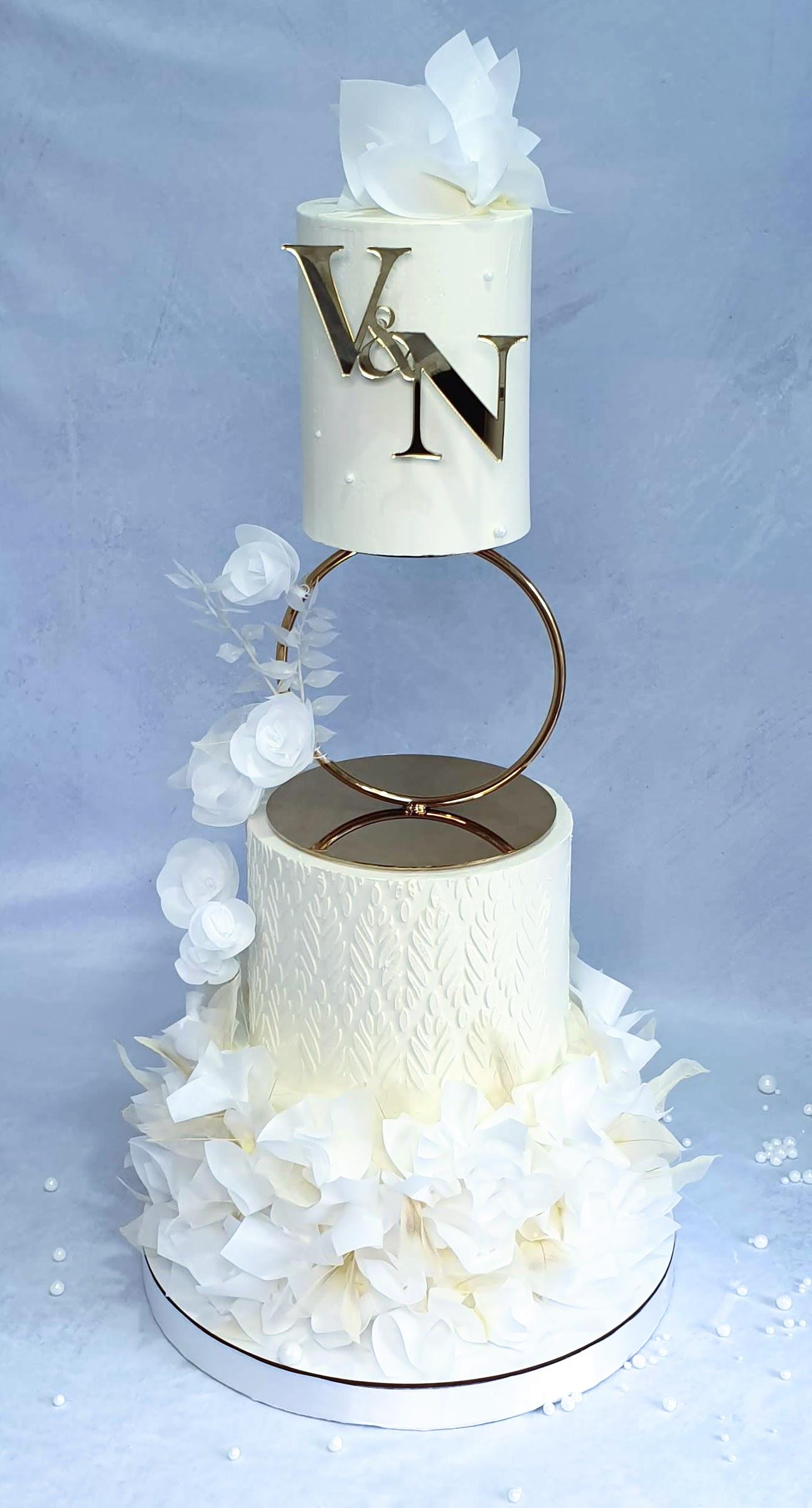 Three-tier white wedding cake with textured buttercream base, bronze V&N topper