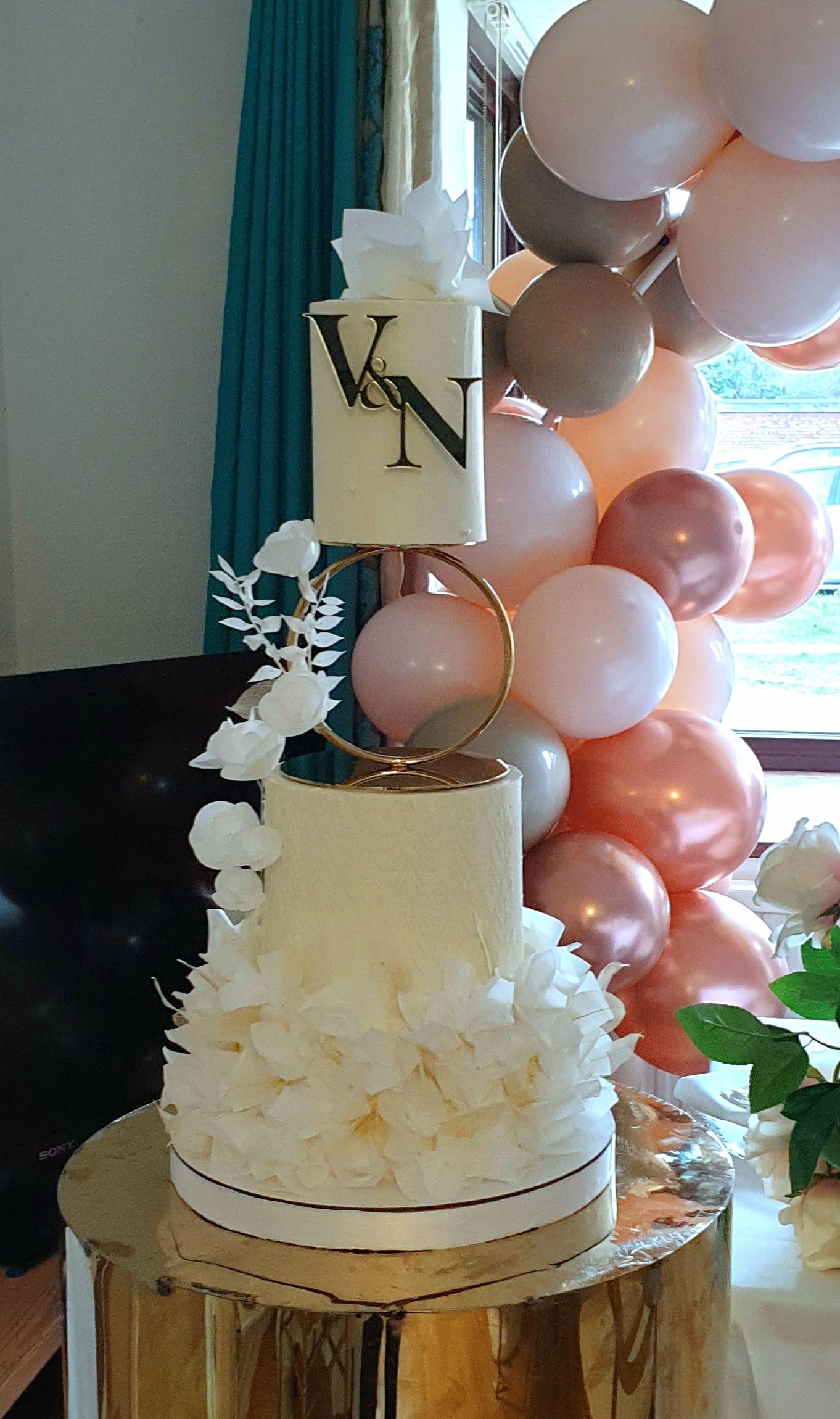 Three-tier wedding cake with textured cream buttercream, wafer paper flowers, and rose gold balloon installation