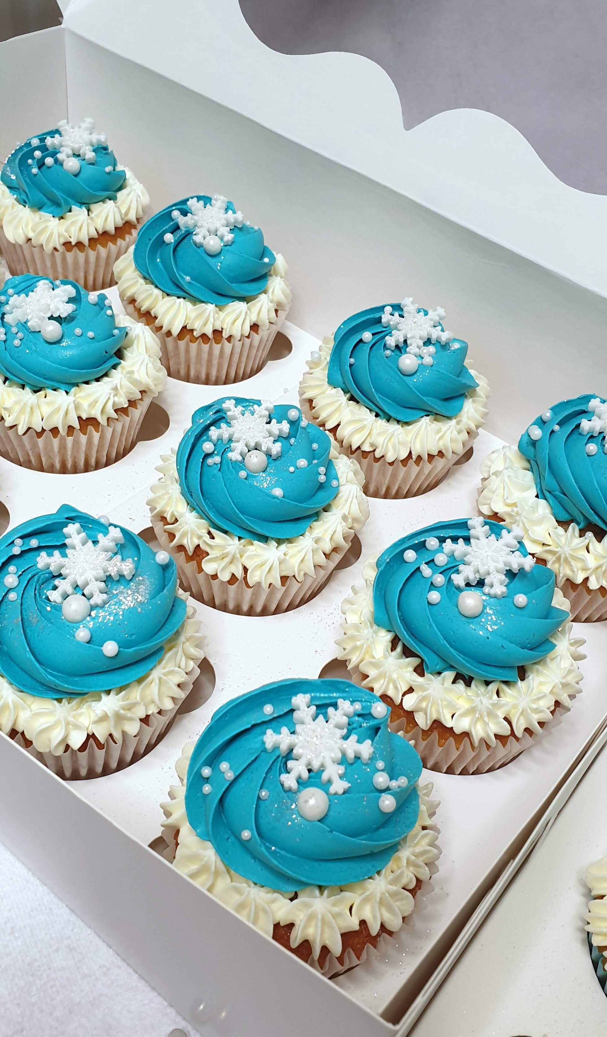 Nine turquoise buttercream cupcakes with cream piped bases, topped with white sugar snowflakes and pearl sprinkles
