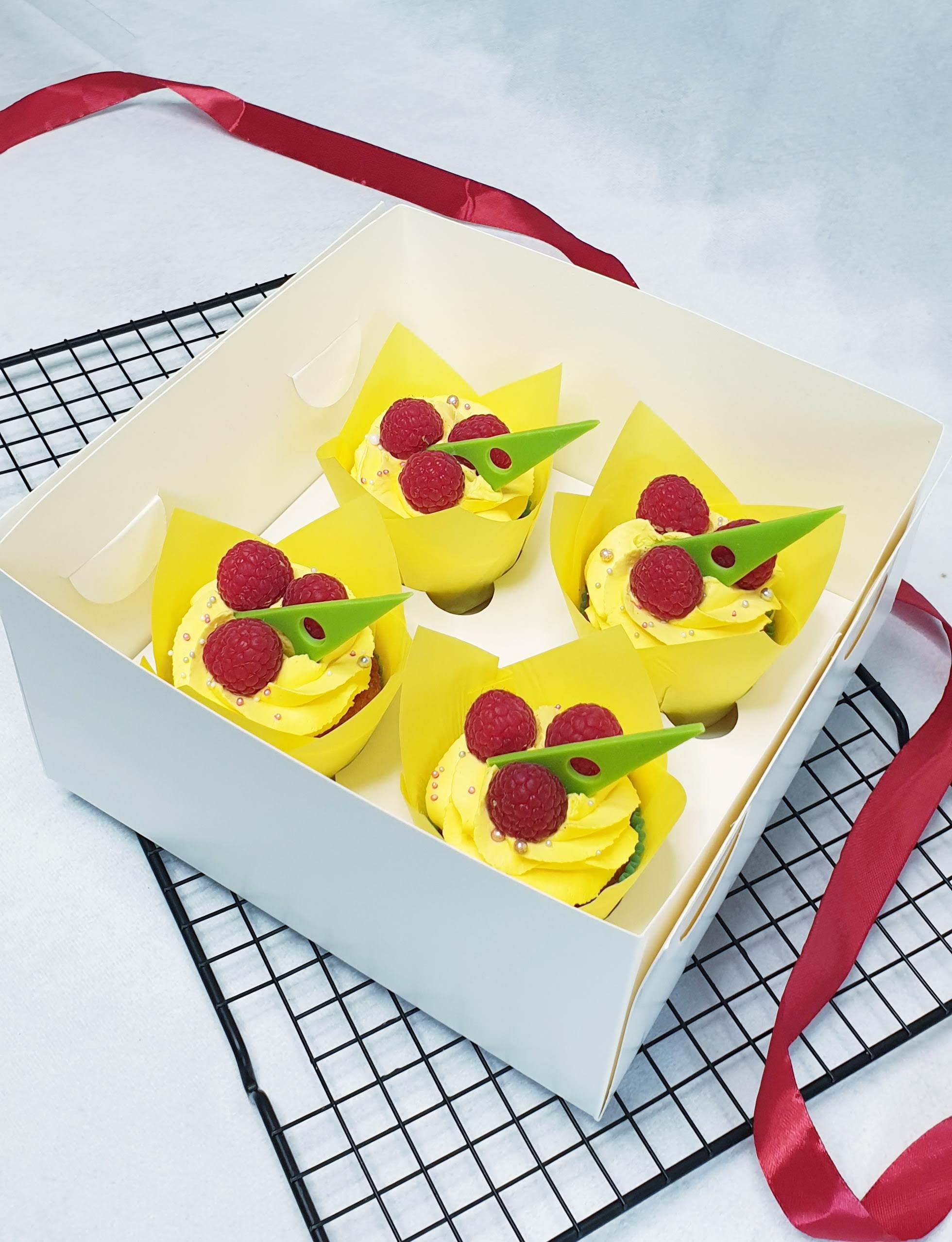 Four cupcakes with bright yellow buttercream frosting, topped with fresh raspberries and green wafer paper decoration
