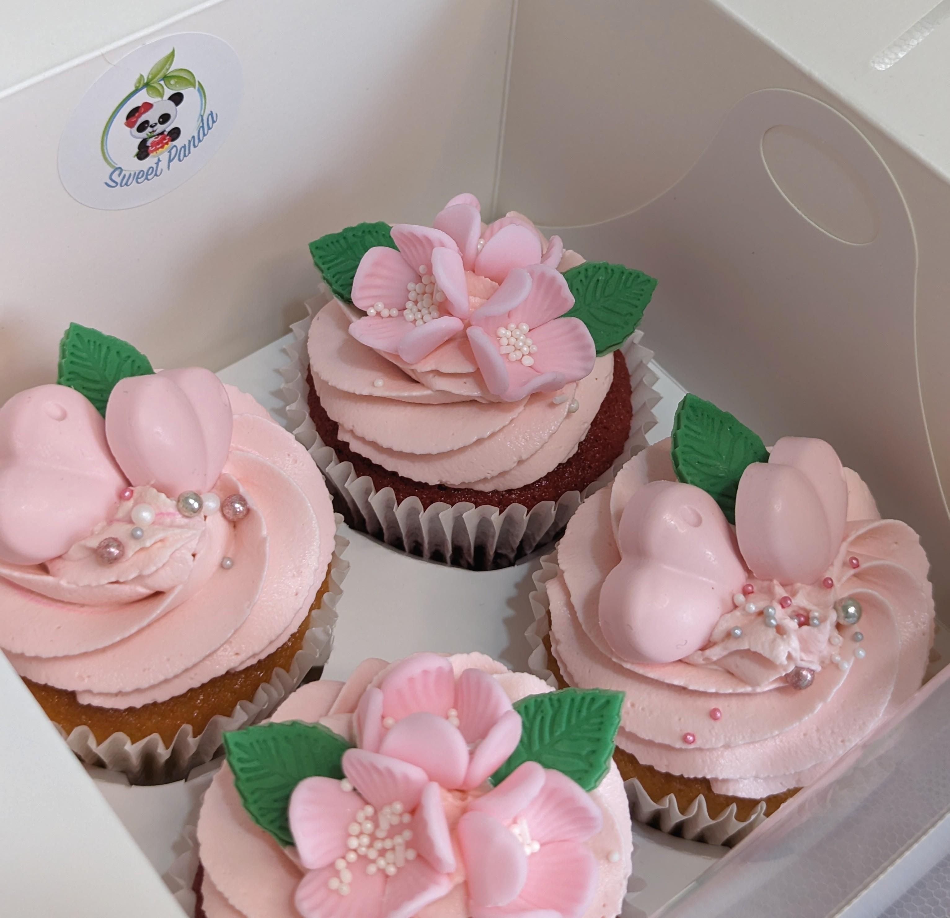 Four decorated cupcakes with pink buttercream frosting, fondant sugar flowers in pink with pearl centres