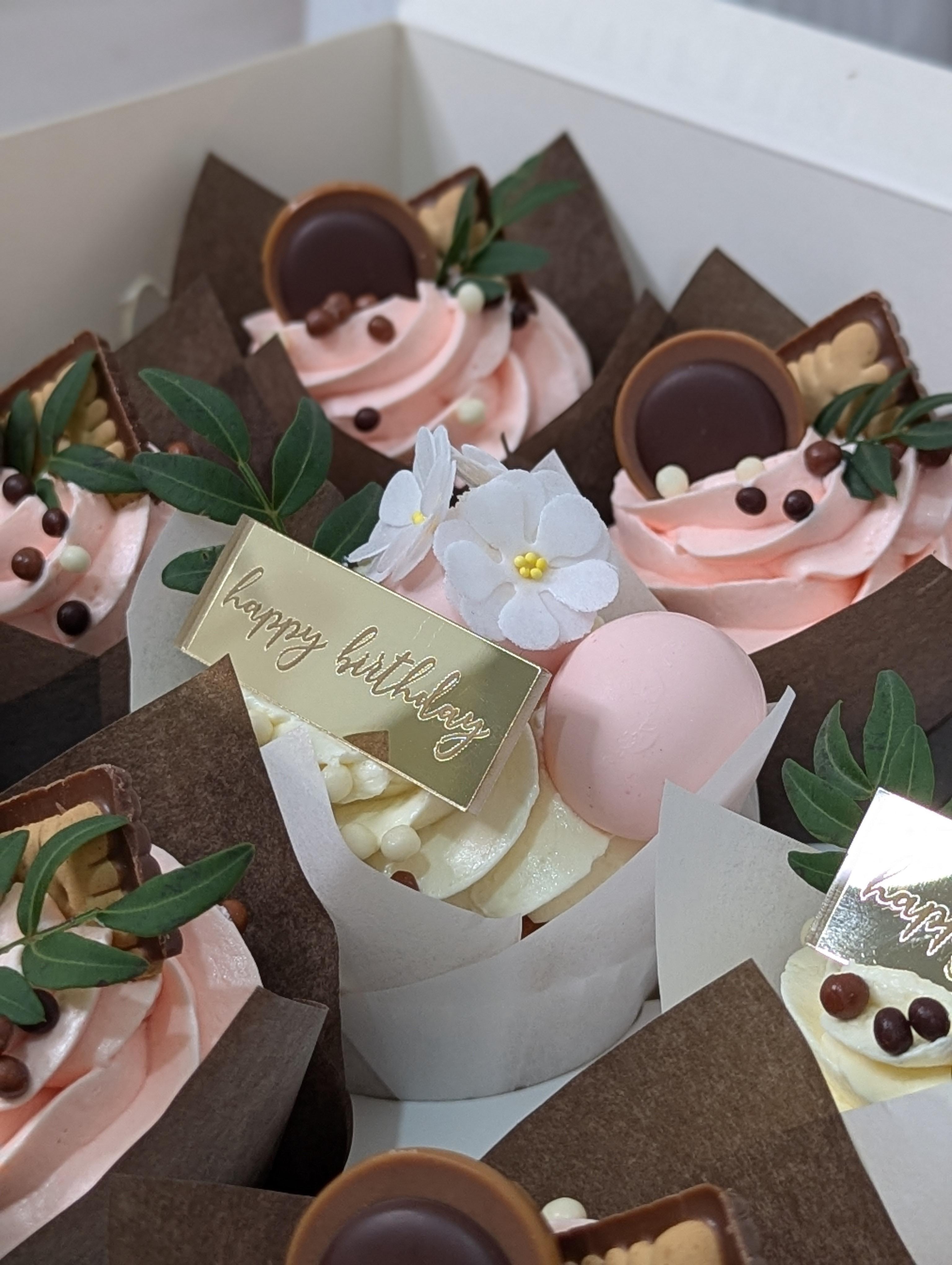 Collection of pink and cream cupcakes with chocolate discs, white sugar flowers