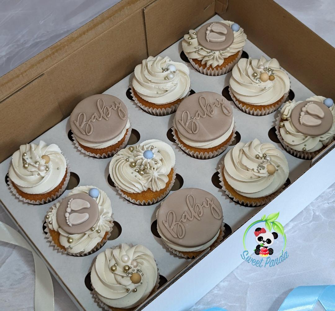 Twelve baby shower cupcakes with cream and beige swirled buttercream, decorated with pearl sprinkles and pale blue accents