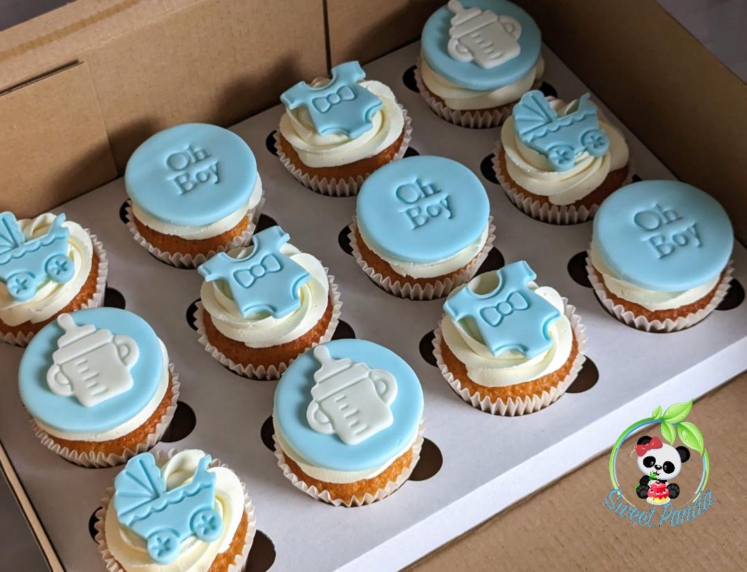 Twelve baby shower cupcakes with light blue fondant toppers decorated with bottle and pram designs, featuring 'Oh Boy' text