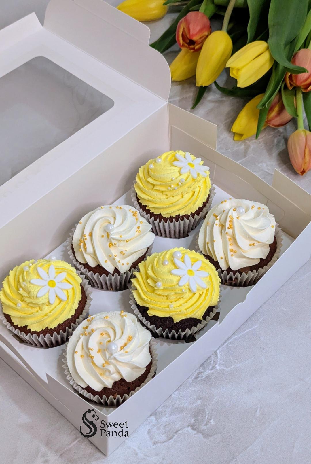 Six chocolate cupcakes with yellow and white buttercream frosting, decorated with white daisy flowers and gold sprinkles