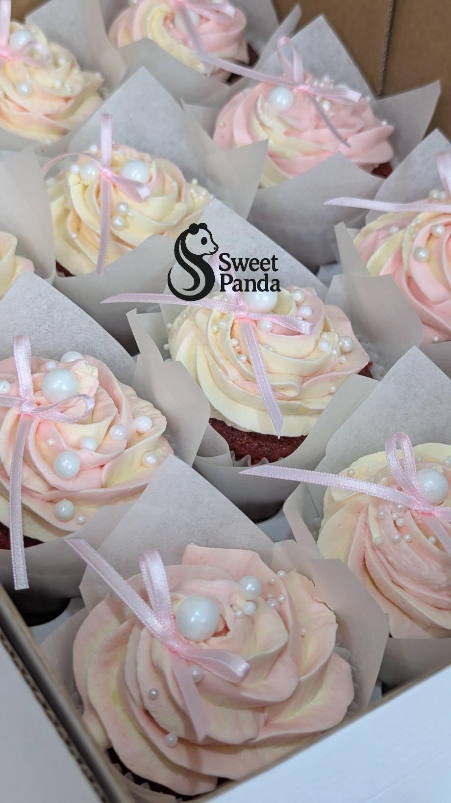 Box of cupcakes with swirled pink and cream frosting, white pearl decorations and pink ribbon bows