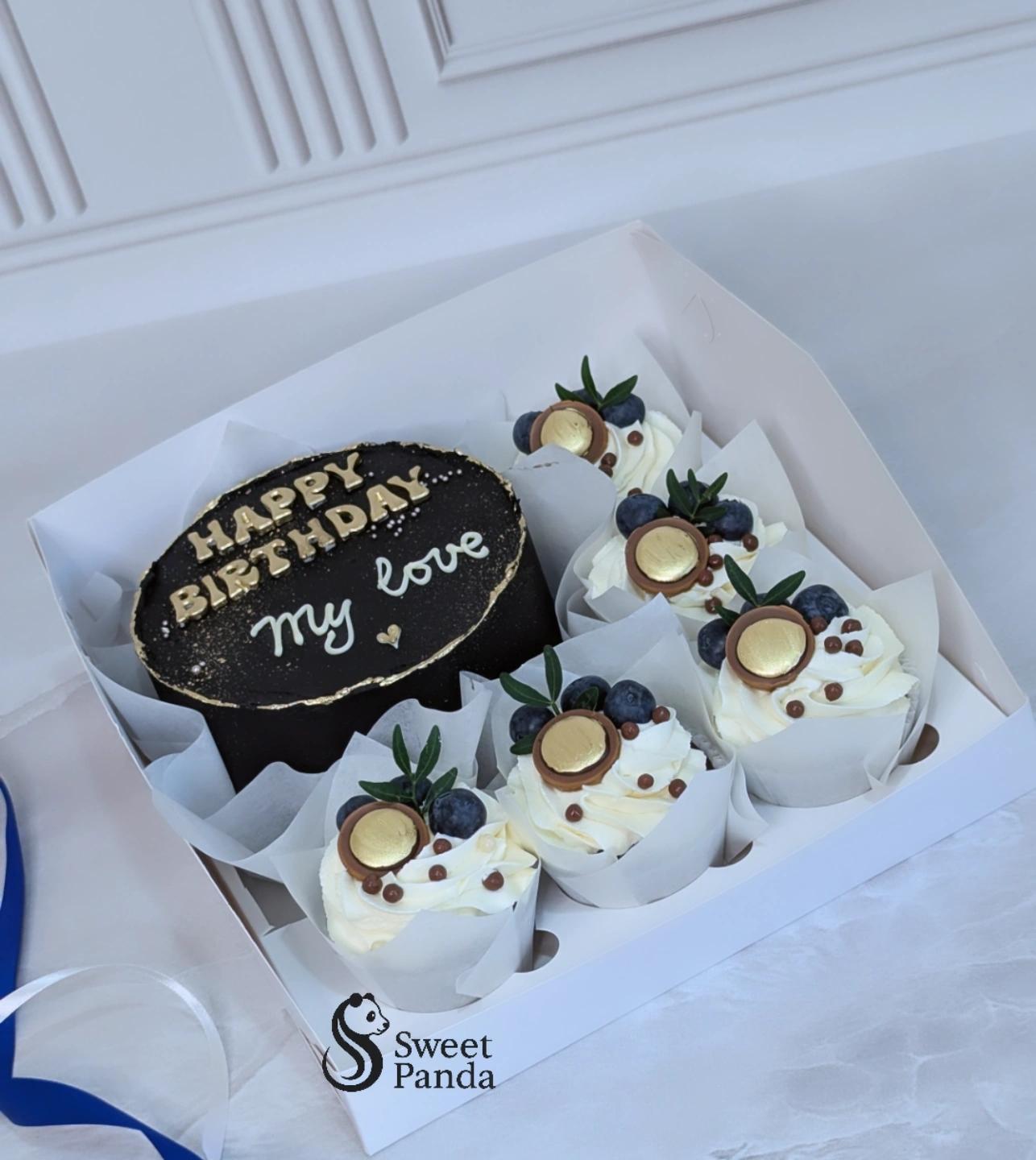 Black and white birthday bento box with chocolate cake, five cream cupcakes topped with blueberries
