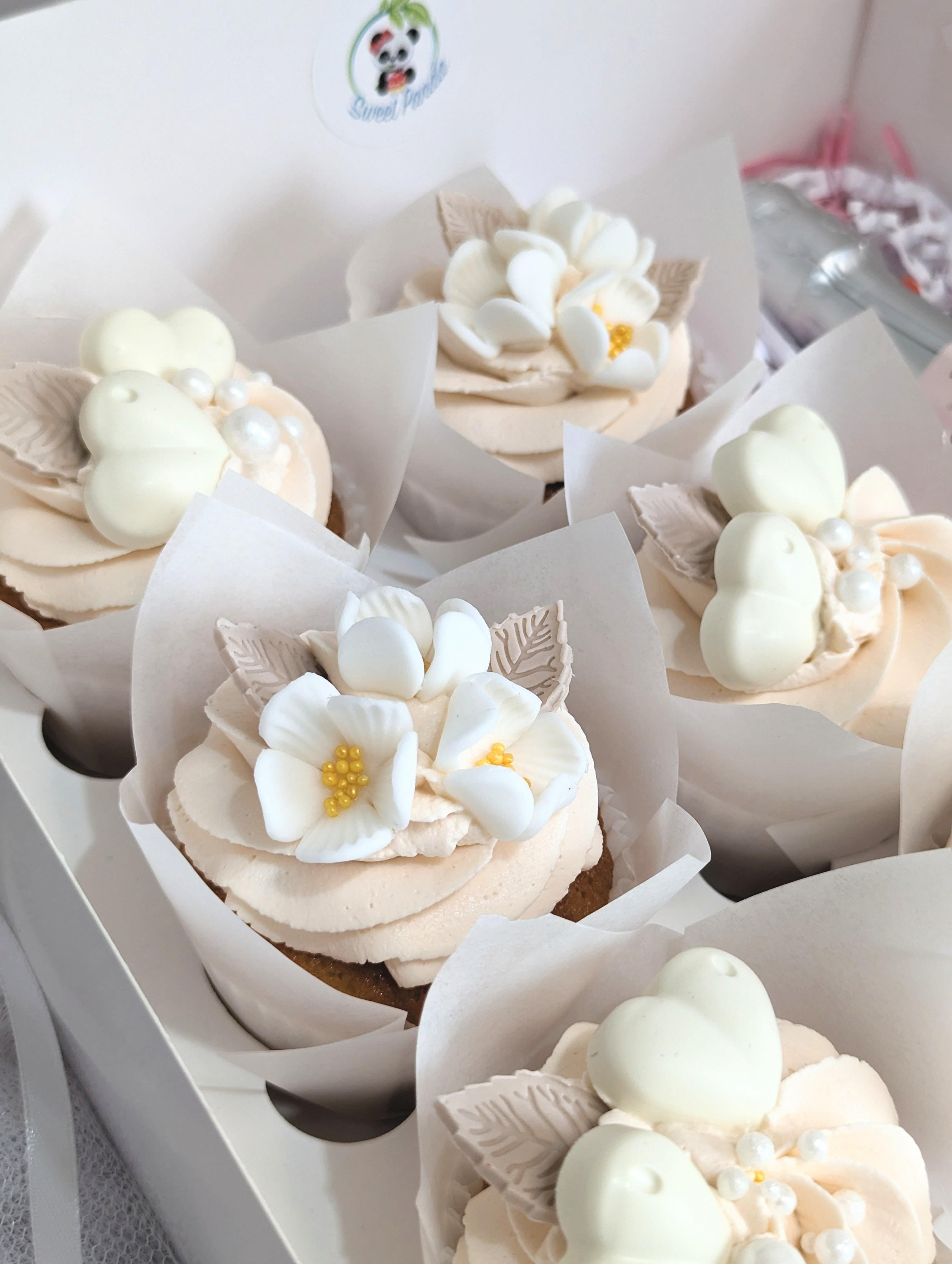 Box of bento cakes with cream buttercream frosting topped with white sugar flowers and metallic gold centres