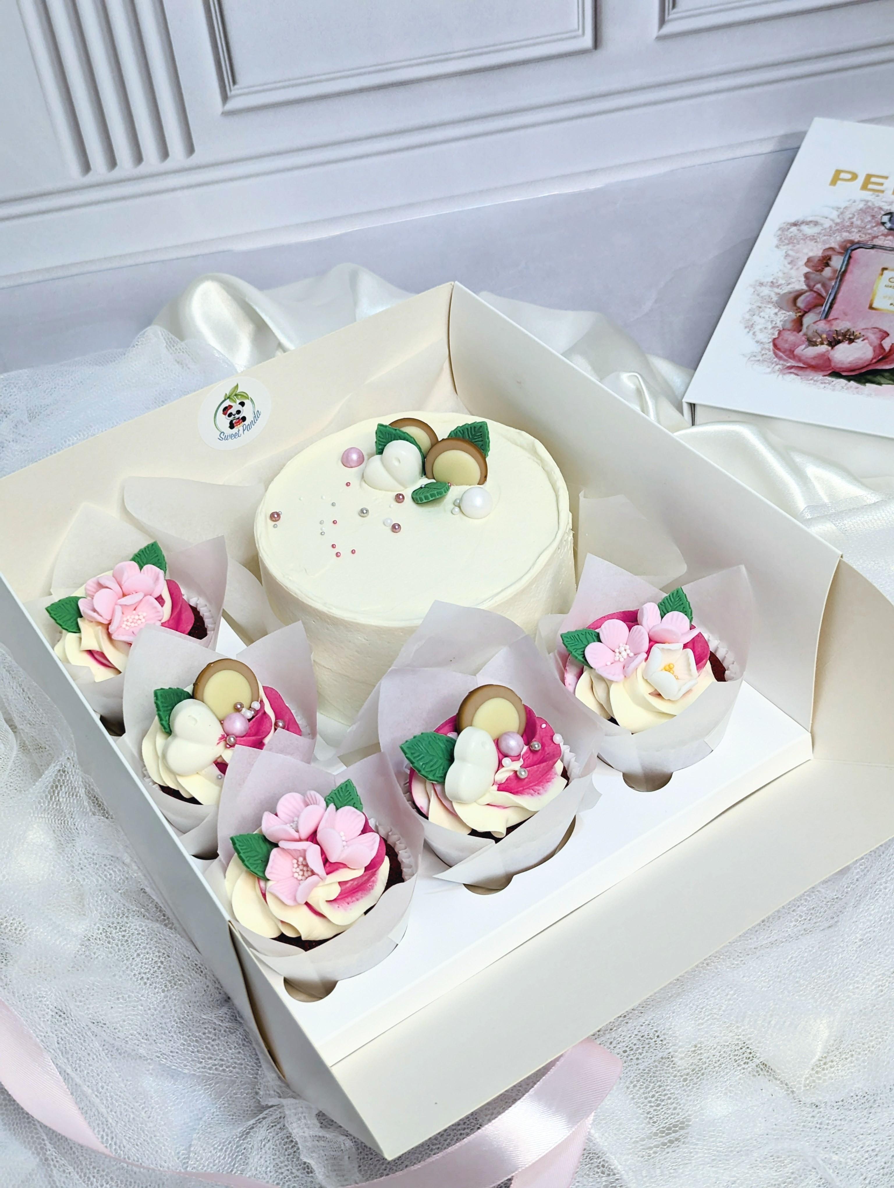 Bento box with cream cake and four cupcakes decorated with pink and white sugar flowers, green leaves
