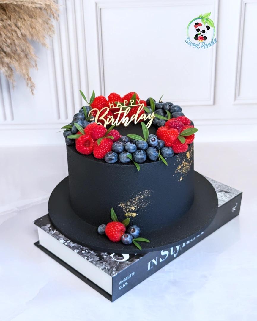 Two-tier black velvet cake decorated with fresh raspberries, blueberries and green leaves