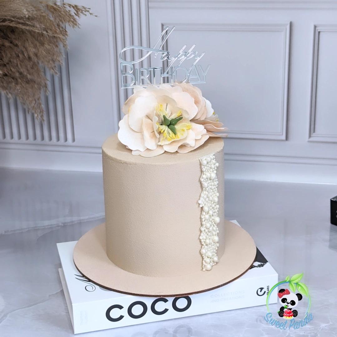 Single-tier beige velvet cake with cream sugar flowers, pearl detail stripe and silver birthday topper on white cake board