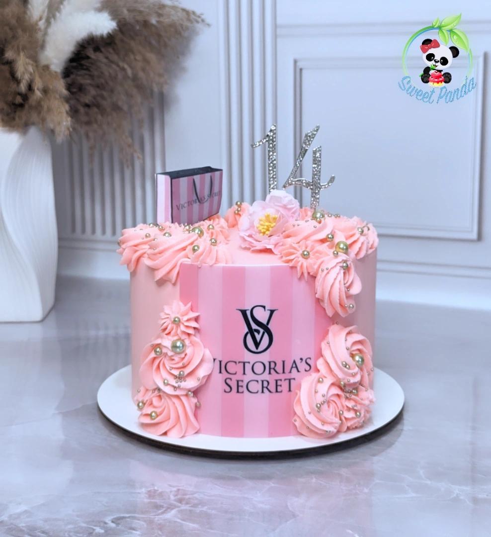 Pink single-tier cake with Victoria's Secret logo, decorated with piped rosettes, gold pearl sprinkles