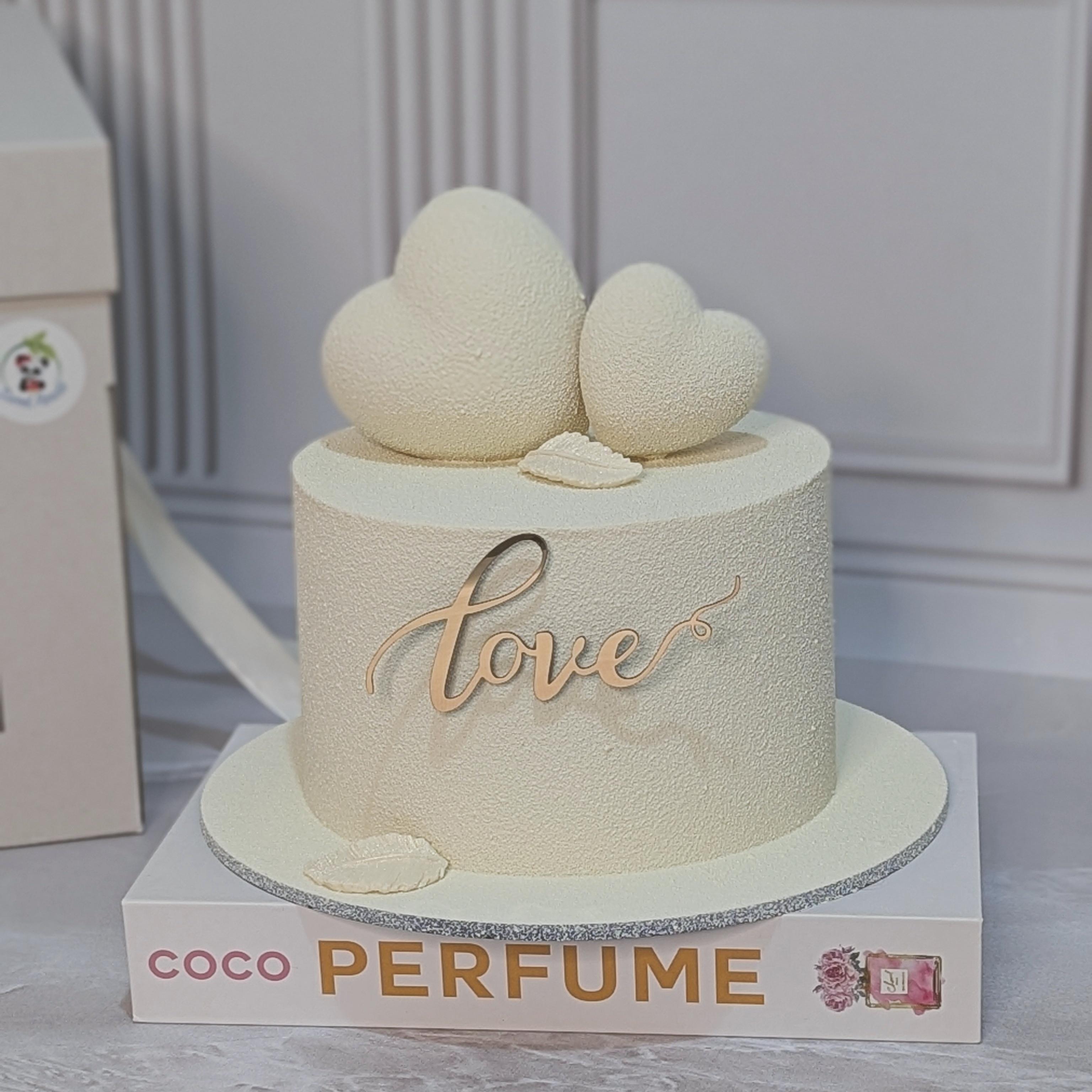 Cream fondant cake with 'love' inscription and two heart toppers on silver-trimmed base