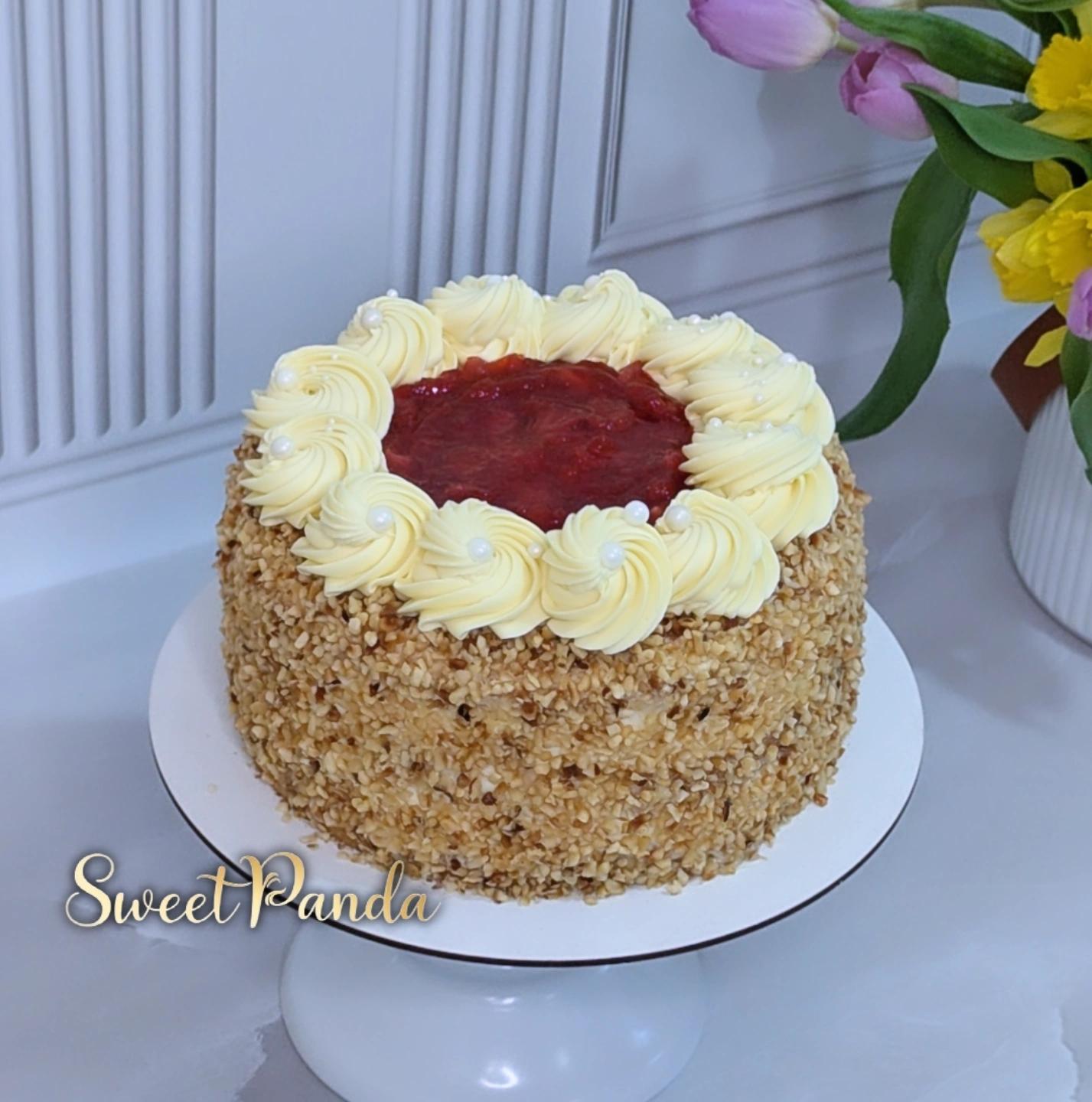 Round layer cake with toasted nut or cereal coating, cream piped rosettes border, and deep red jam or fruit centre
