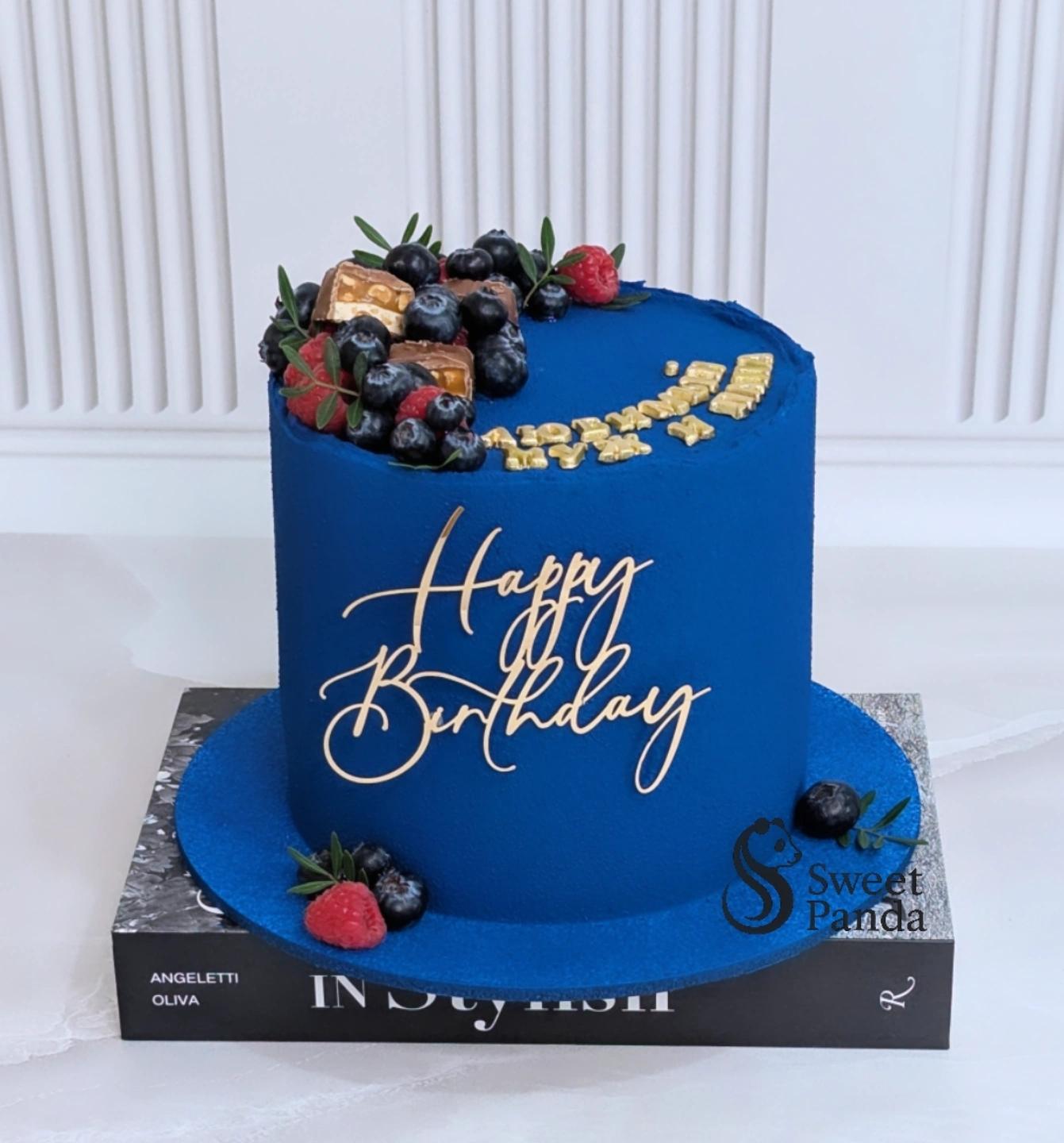 Blue fondant celebration cake with gold script 'Happy Birthday', topped with fresh raspberries