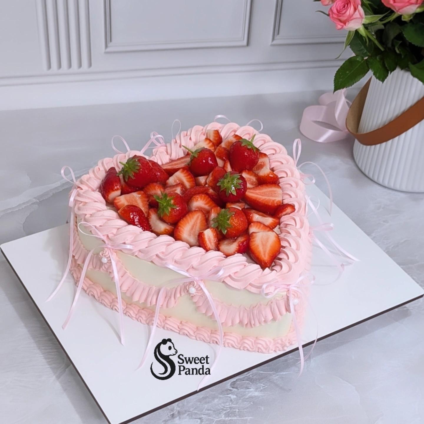Heart-shaped cake with pink piped Lambeth-style frosting, topped with fresh strawberries and pistachio leaves