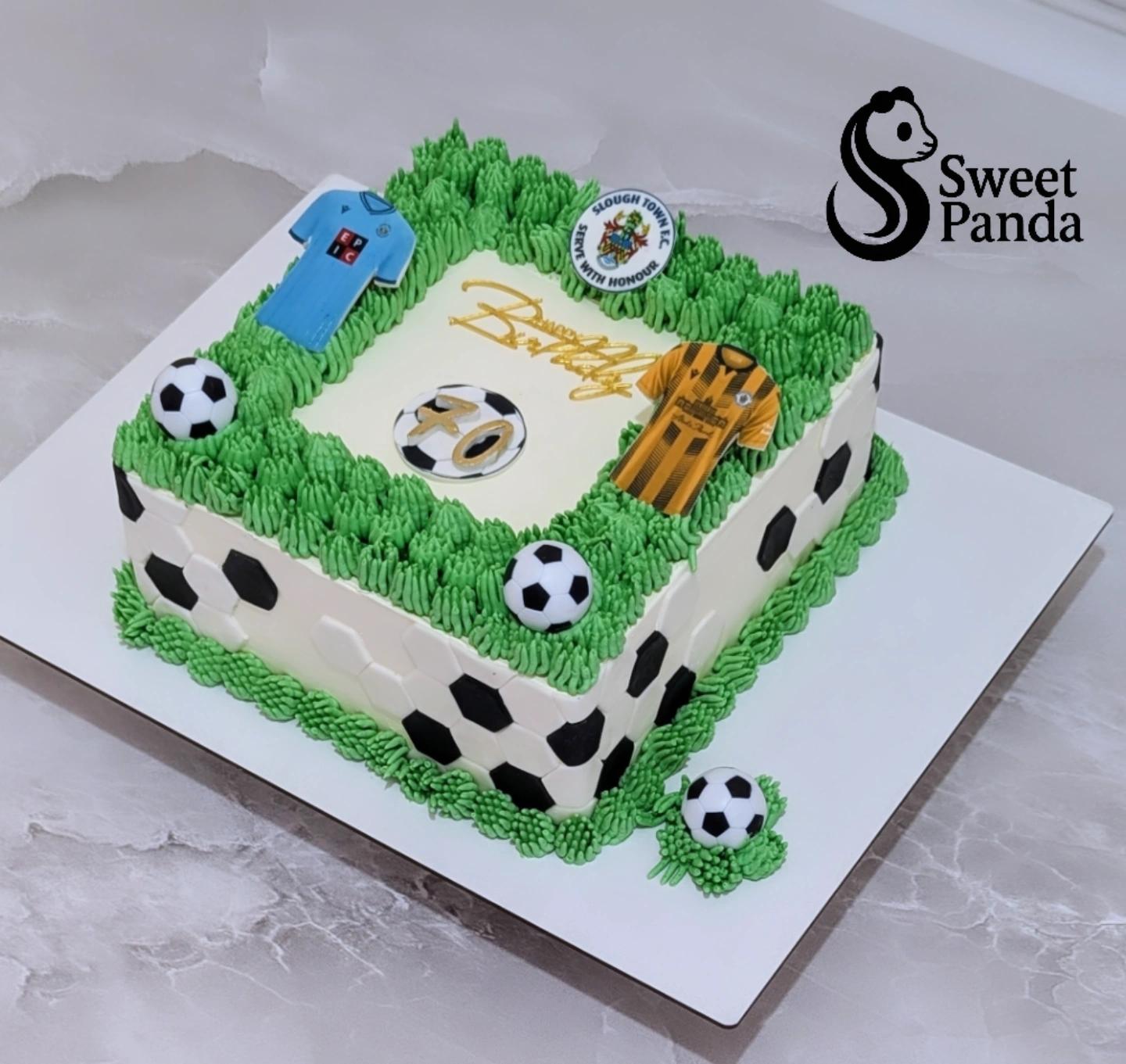 Two-tier football-themed cake with green piped grass border, white fondant base decorated with black football patterns