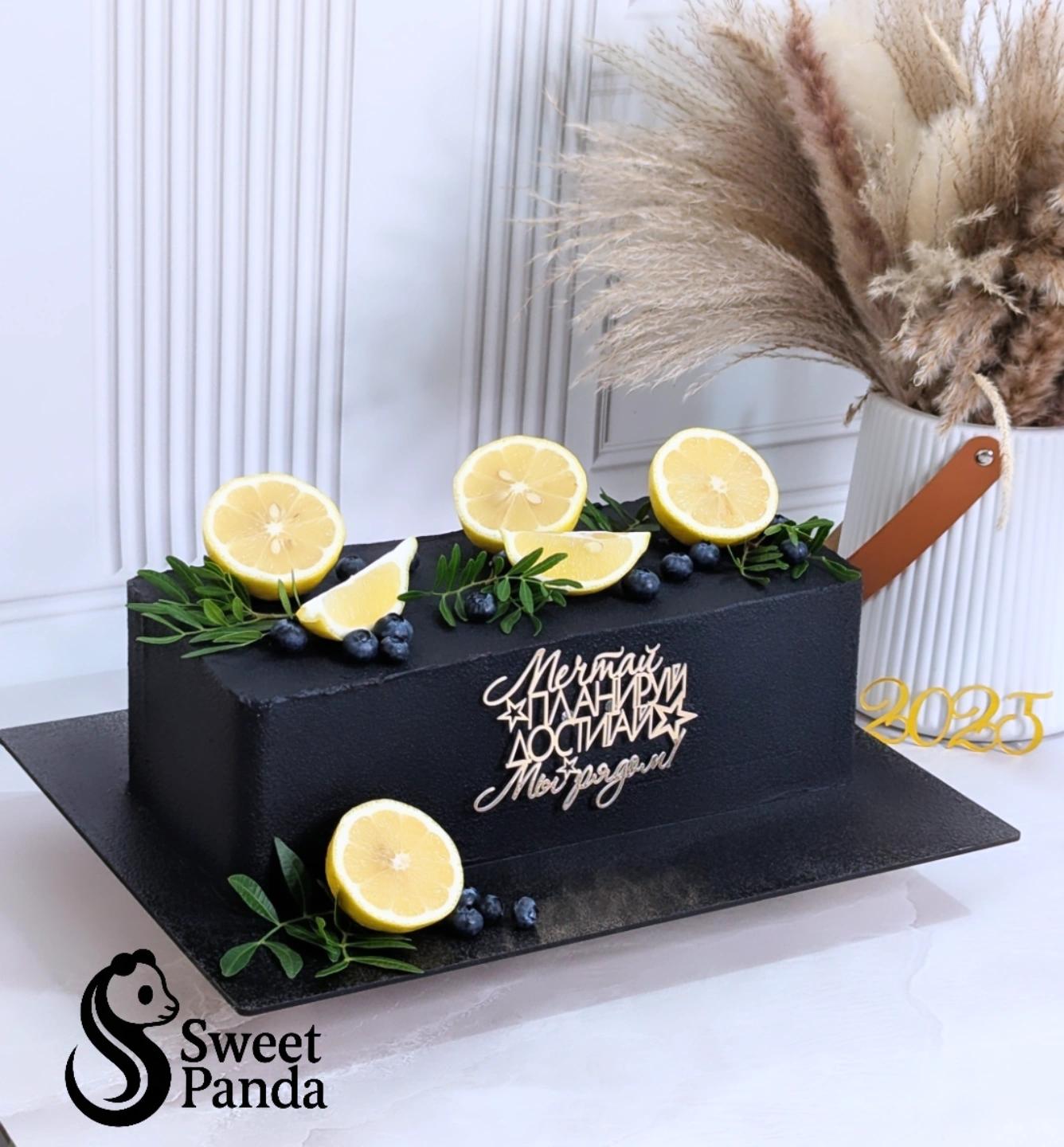 Black ganache cake topped with lemon slices, blueberries and rosemary sprigs, with white piped script and 2025 numeral