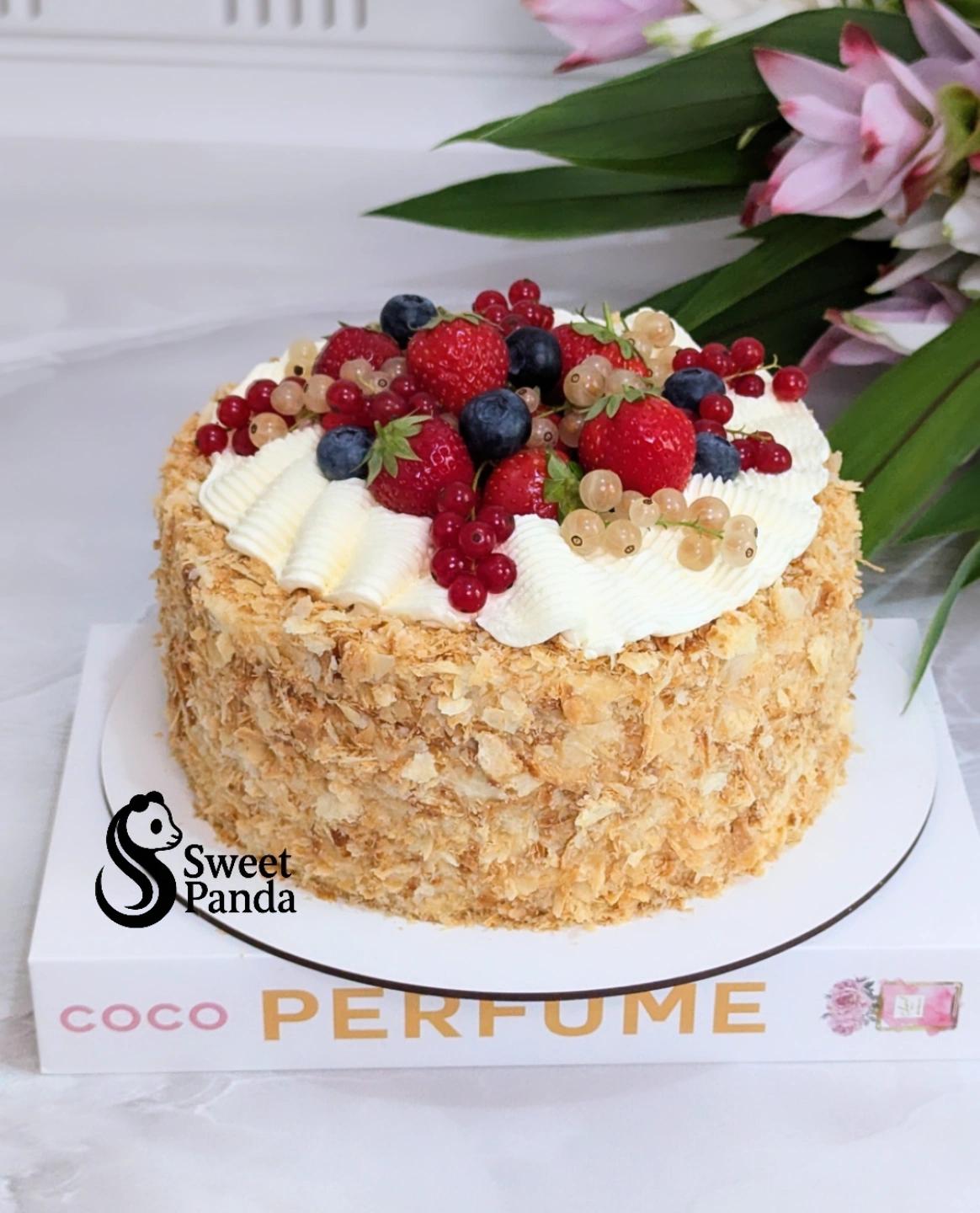Single-tier cake with textured coconut coating, topped with whipped cream and mixed fresh berries including raspberries
