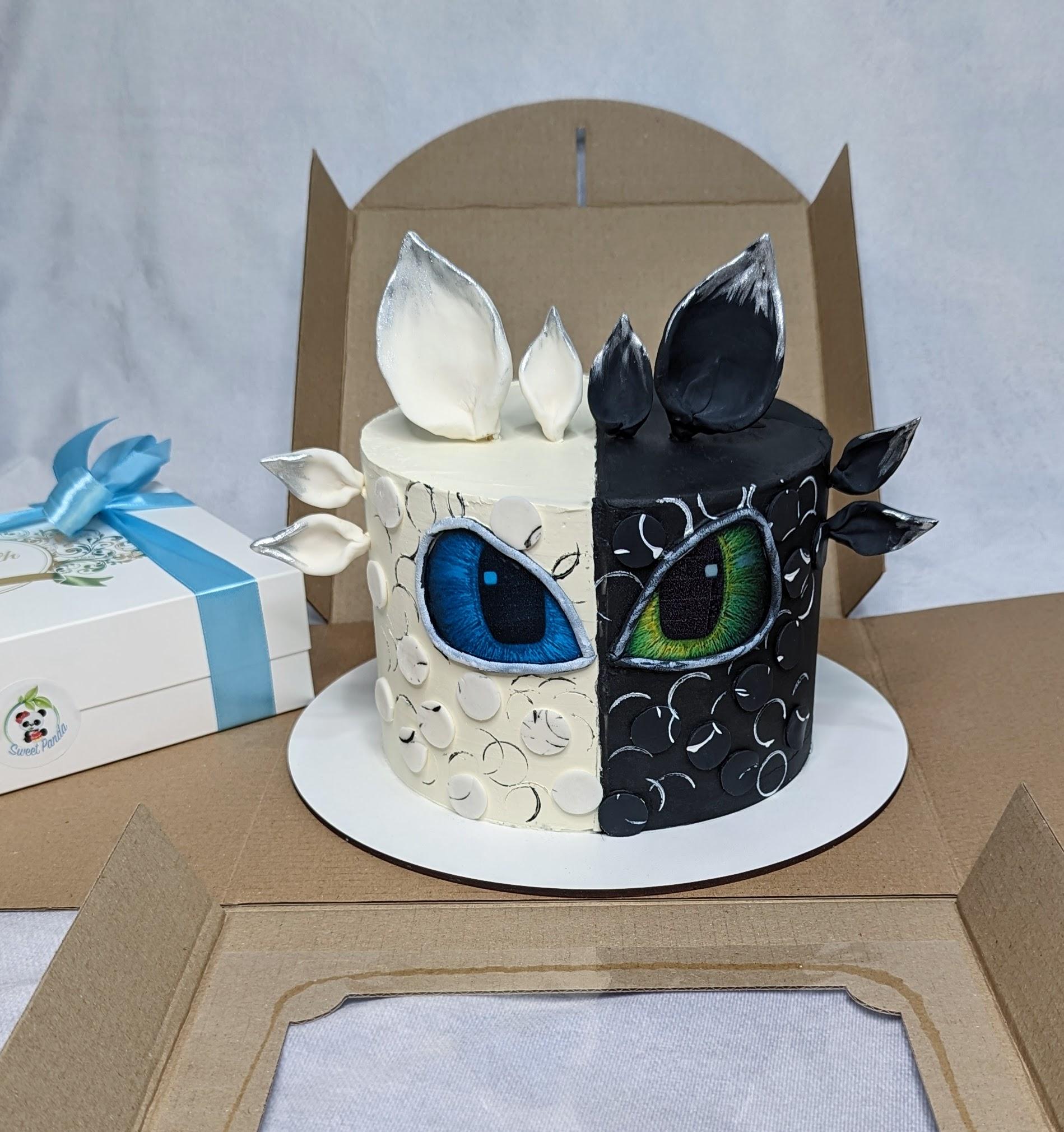 Two-tier cake split between white and black fondant, each side decorated with a large dragon eye