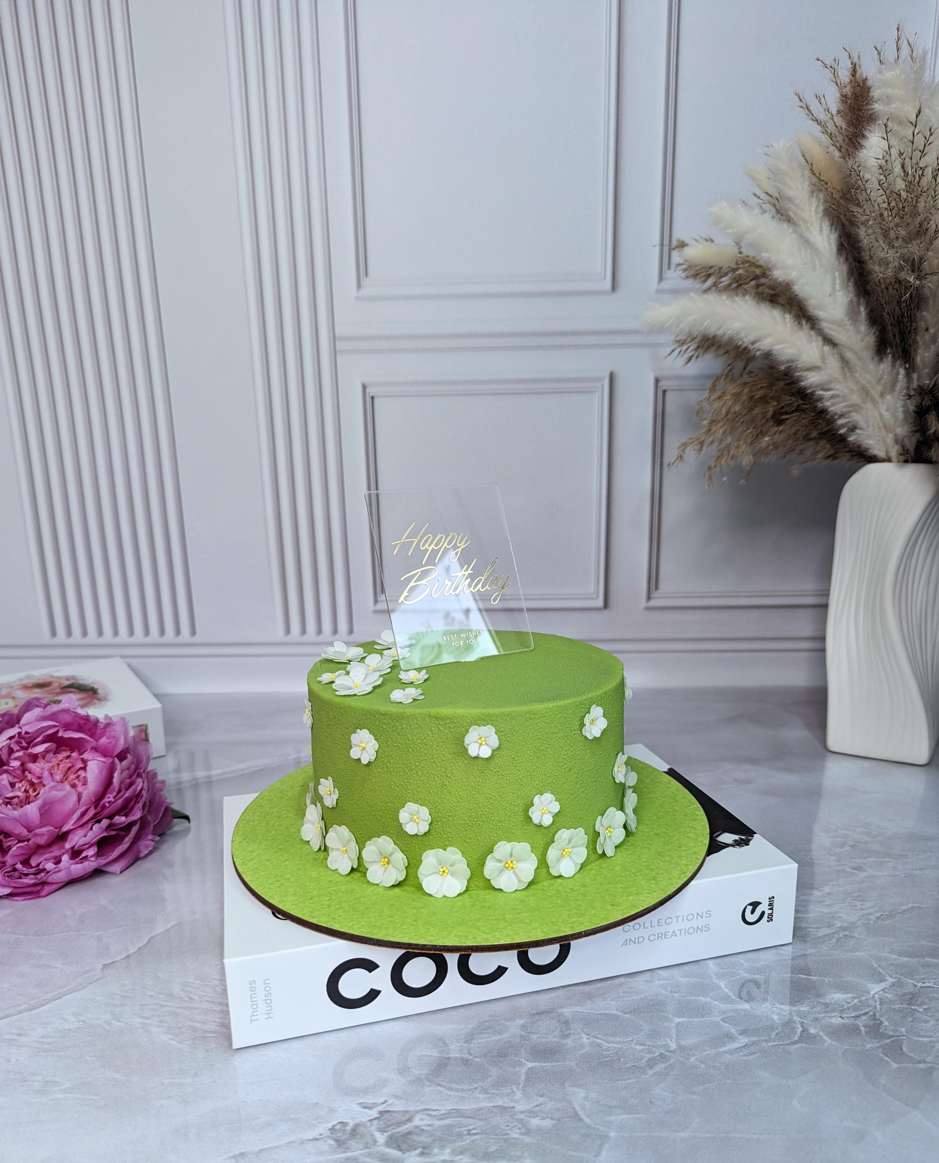 Lime green fondant cake decorated with white fondant flowers and a clear acrylic topper reading 'Happy Birthday'