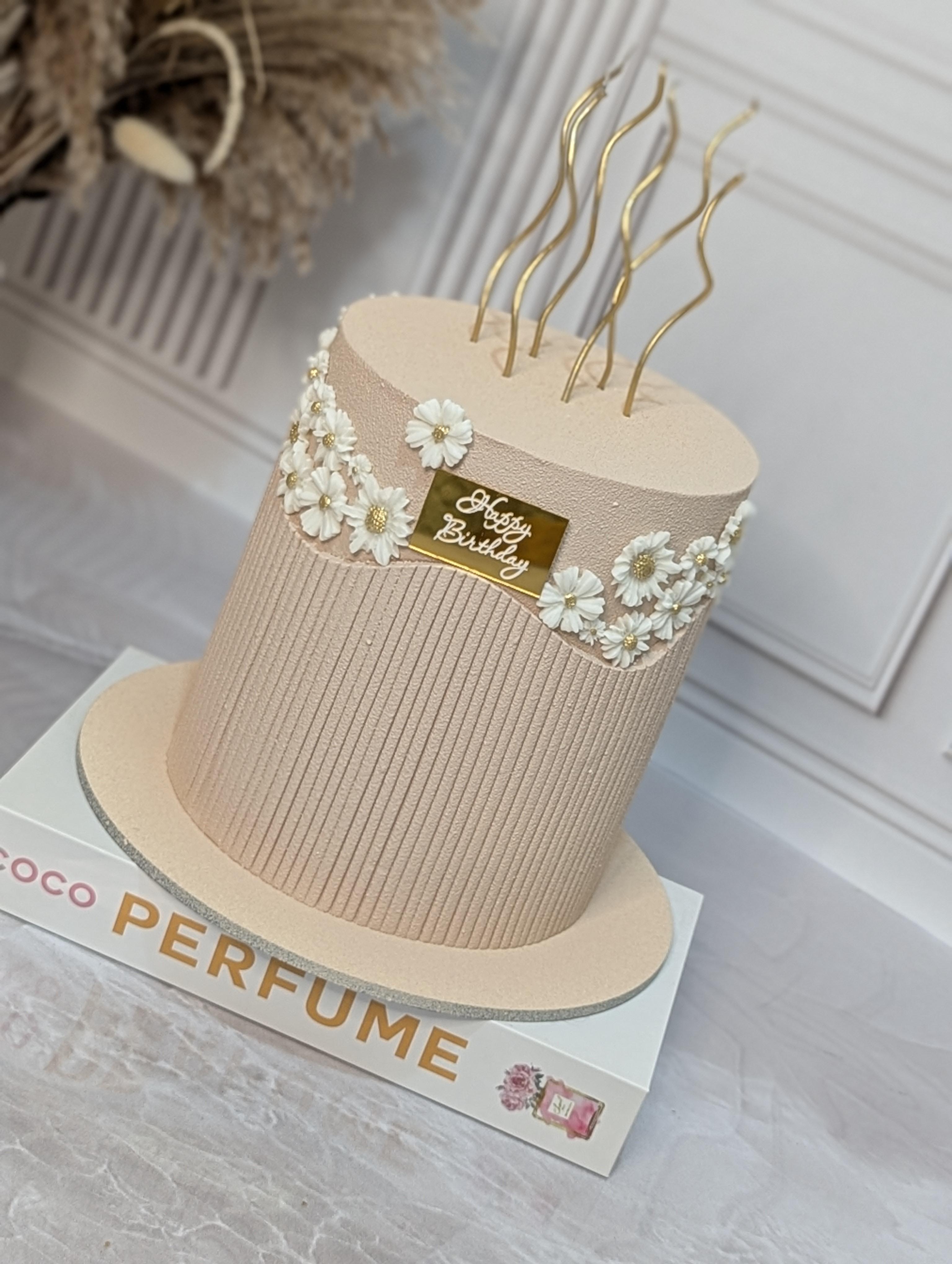 Beige fondant celebration cake with white daisy flowers, gold wavy candles and 'Happy Birthday' plaque on cream base