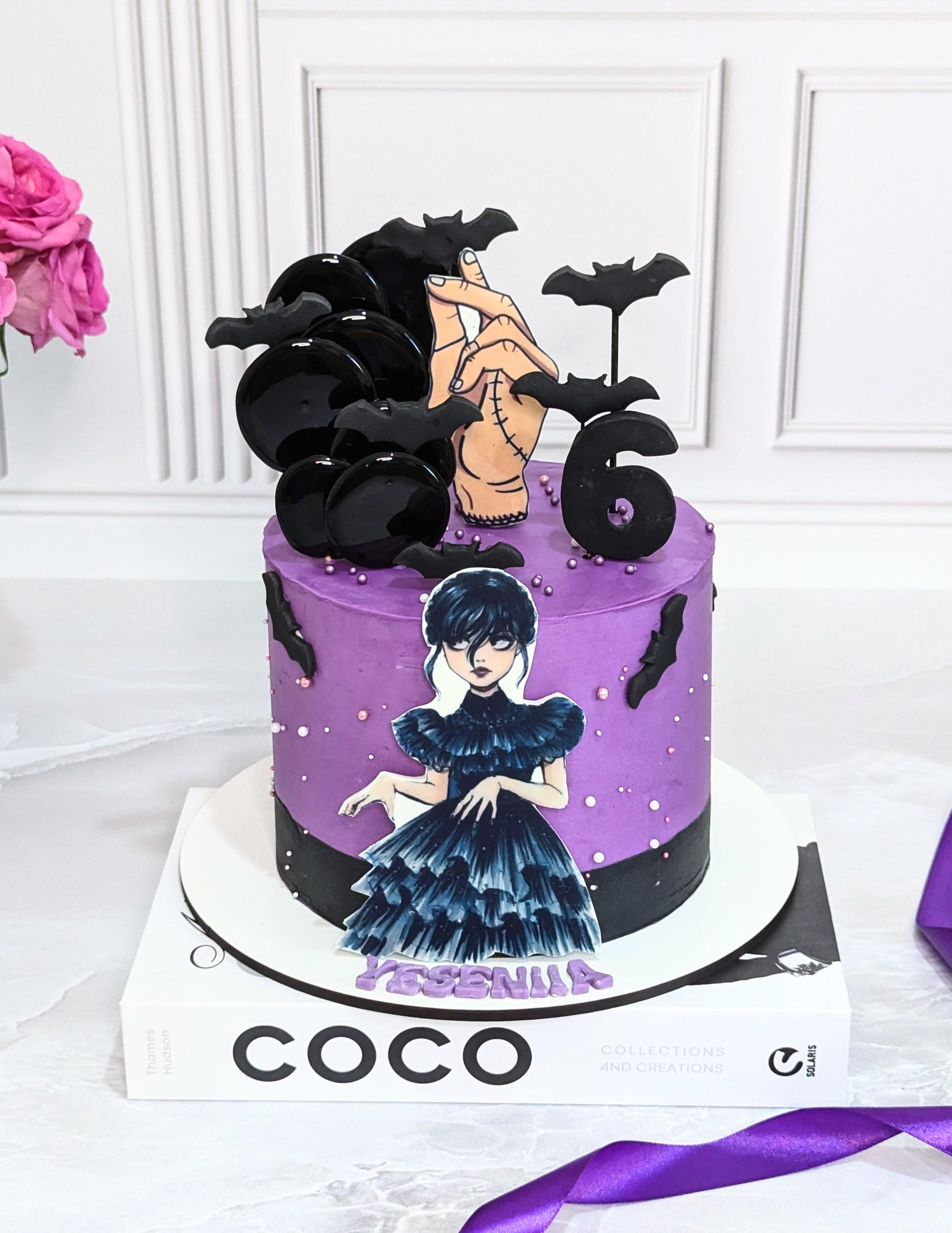 Two-tier purple and black cake decorated with printed Wednesday Addams character images, bat toppers