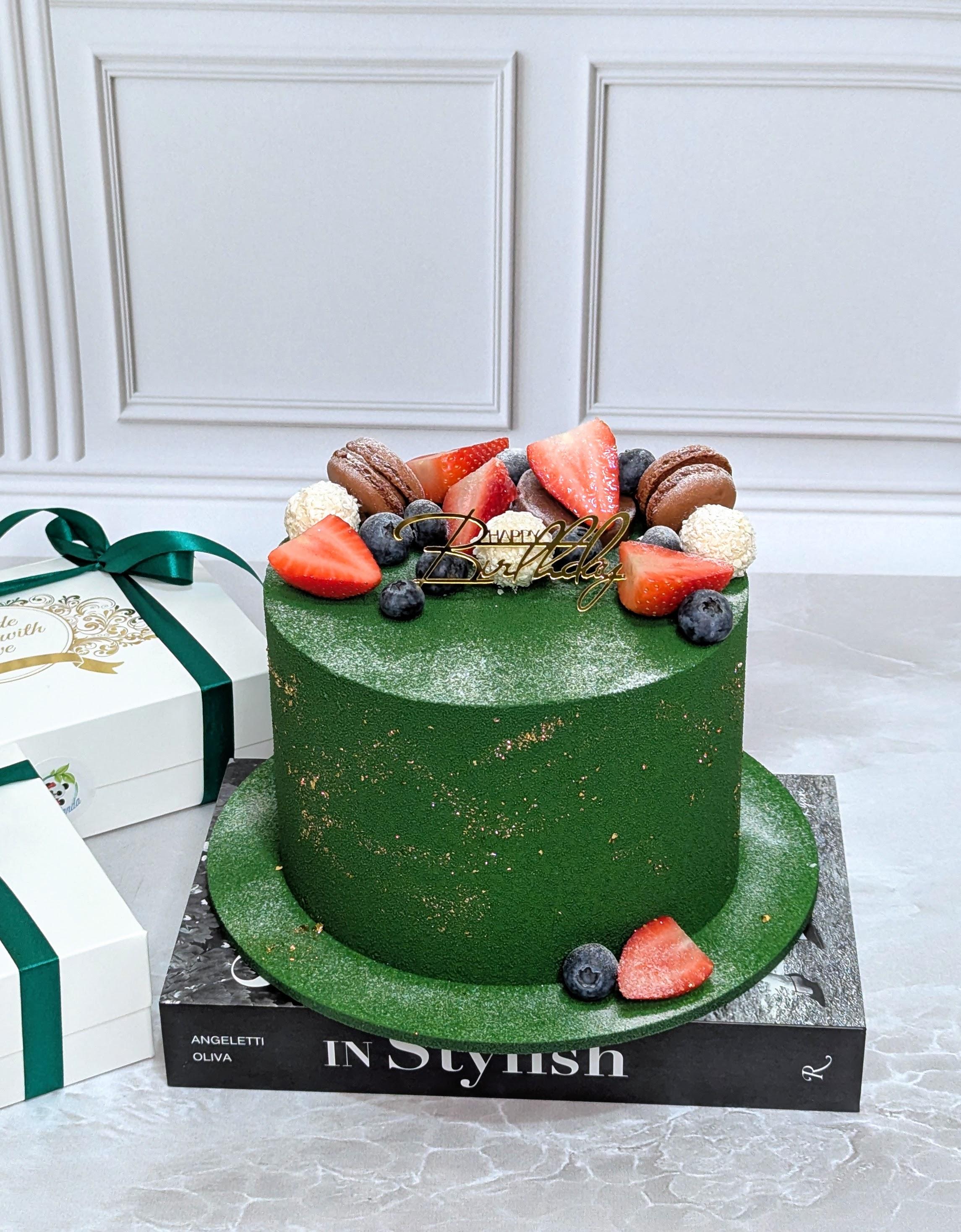 Two-tier green fondant cake with gold flecks, topped with macarons, fresh strawberries