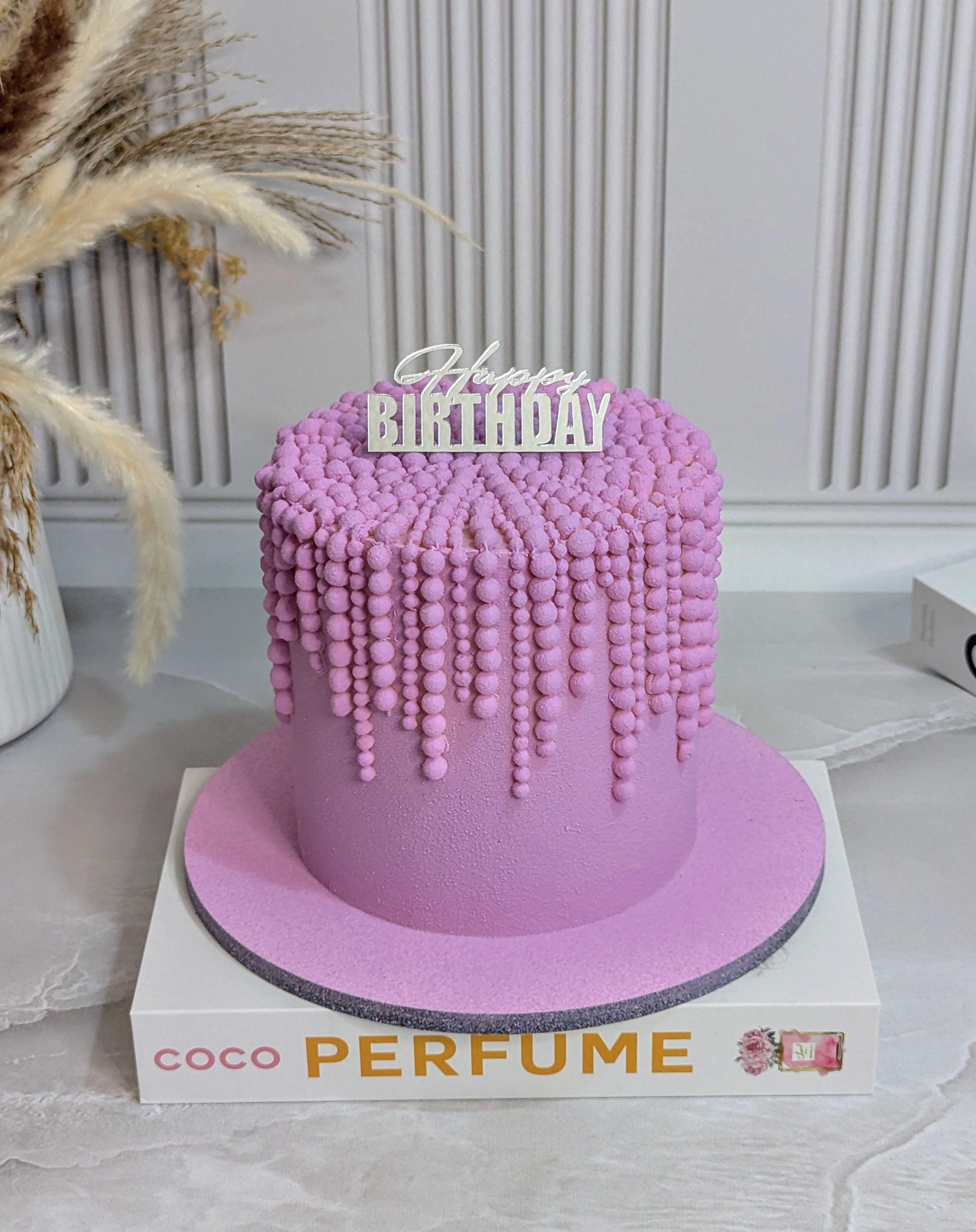 Pink single-tier birthday cake with cascading buttercream balls and 'Happy BIRTHDAY' topper