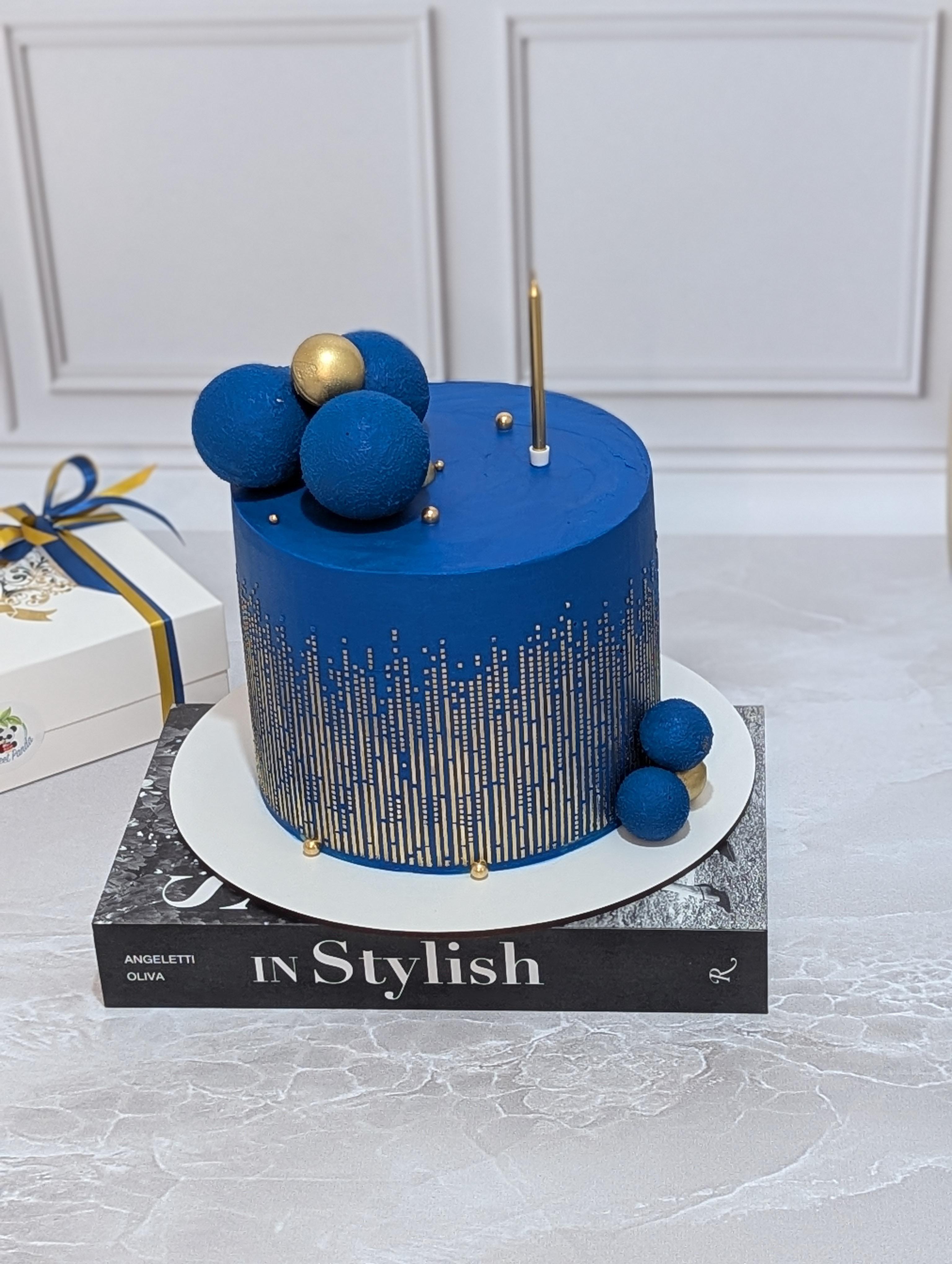 Deep blue fondant cake with vertical striped gold pattern, topped with blue textured spheres and one gold sphere