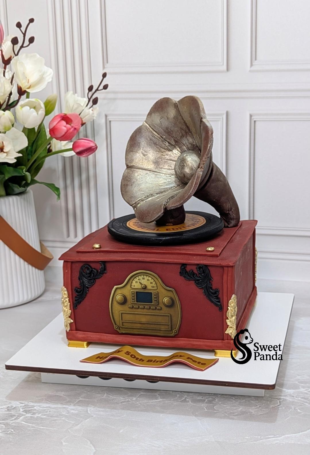 Red fondant cake shaped like a vintage gramophone with metallic brown wings, brass controls and gold accents