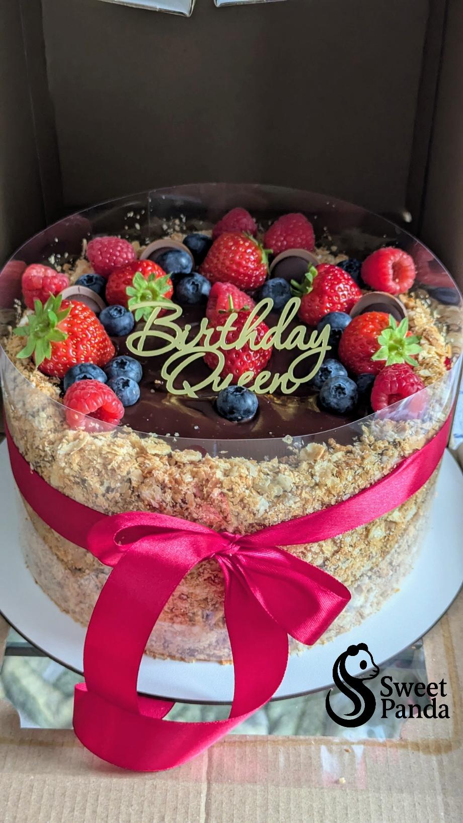 Two-tier cake with chocolate ganache top, cream sides, topped with fresh strawberries, raspberries and blueberries