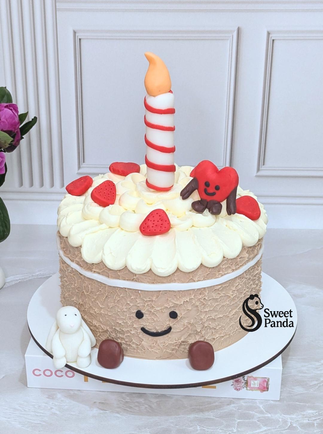 Two-tier beige textured cake with cream piped top, strawberries, chocolate pieces, smiling face