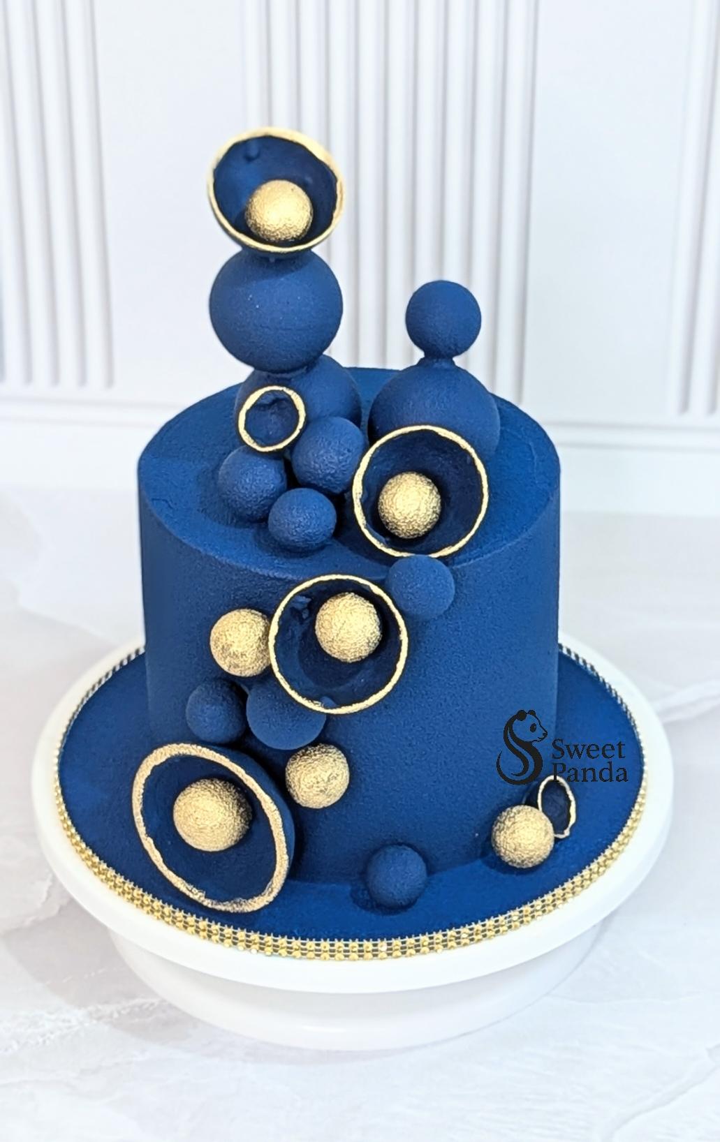 Two-tier deep blue fondant cake with gold geometric rings, spheres and decorative elements