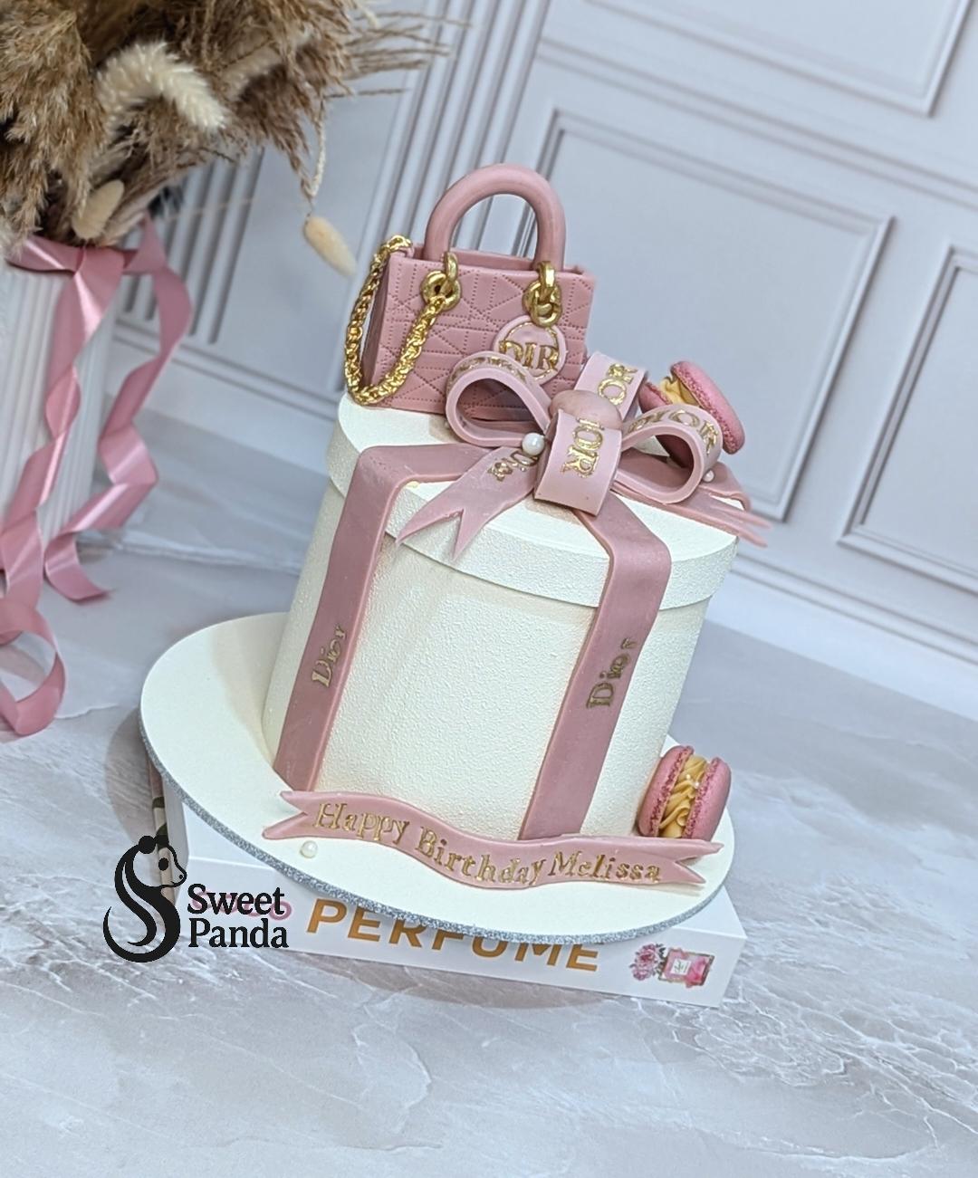 White fondant celebration cake decorated with pink fondant bow, quilted handbag, macarons and gold lettering