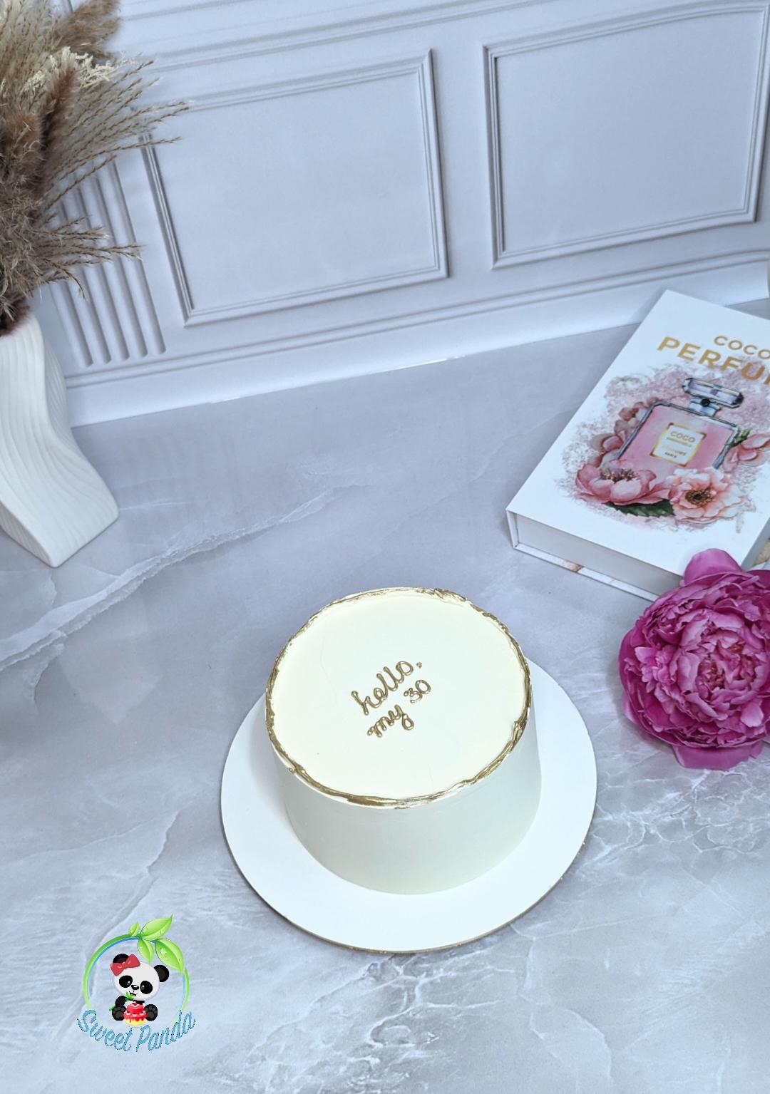 White single-tier cake with gold leaf border and gold script on cream plate