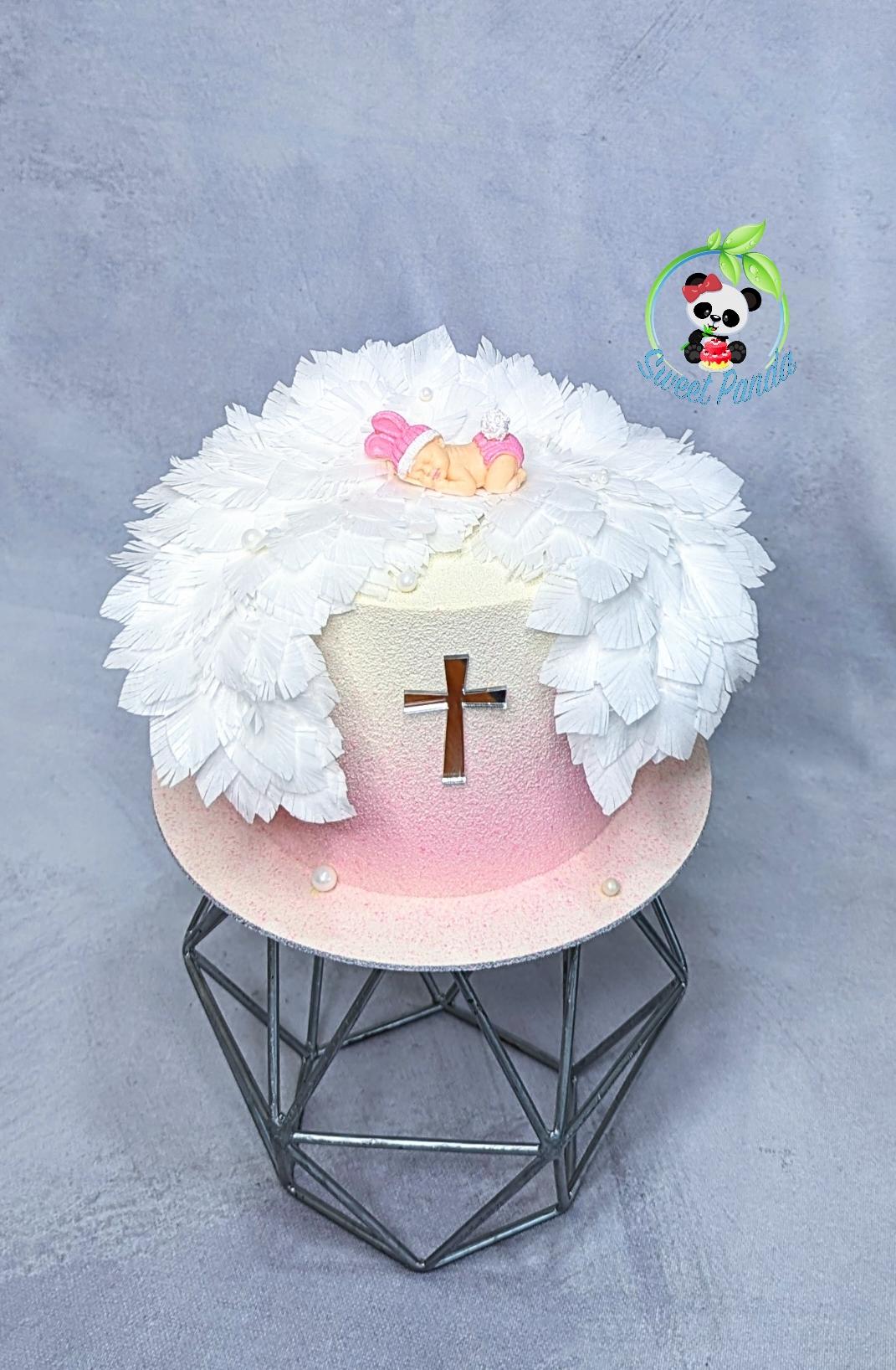 Pink and cream celebration cake with large white wafer paper wings and a sleeping baby figurine on top