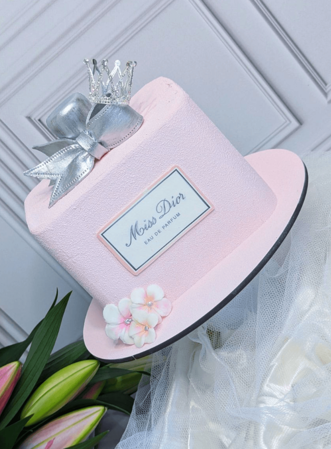 Pink fondant cake shaped like a Miss Dior perfume bottle, topped with a silver crown and bow